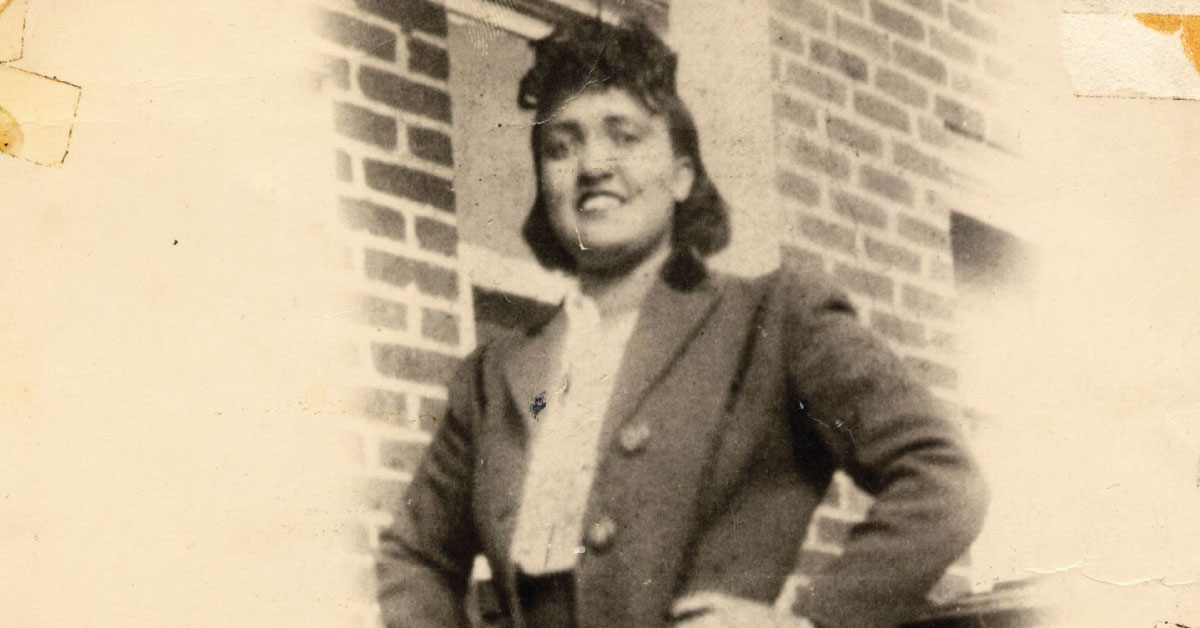 A woman stands confidently in front of a brick wall