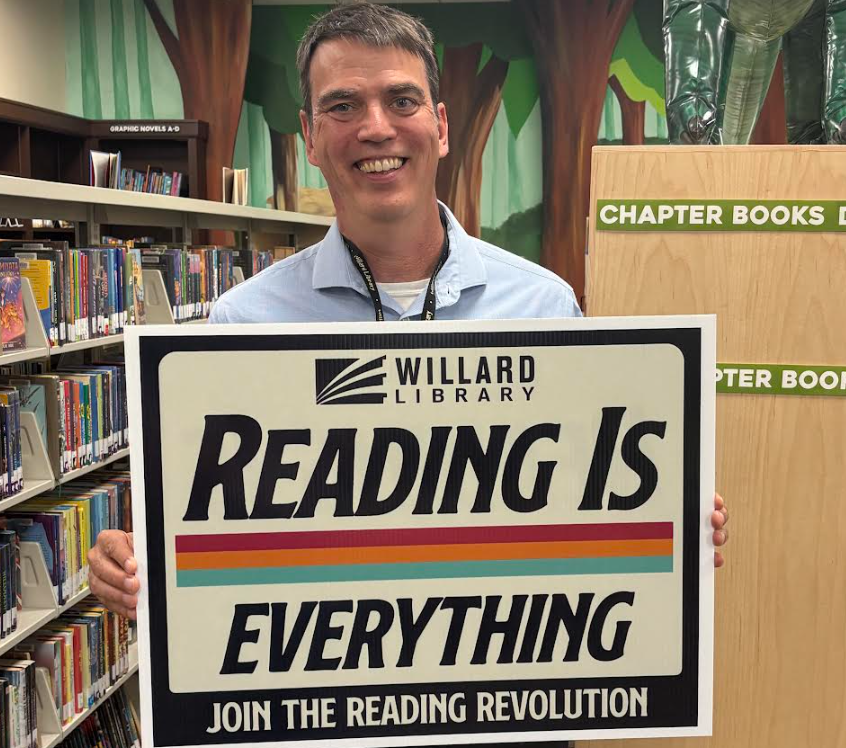 Man holding a sign that says "Reading is everything" in a library